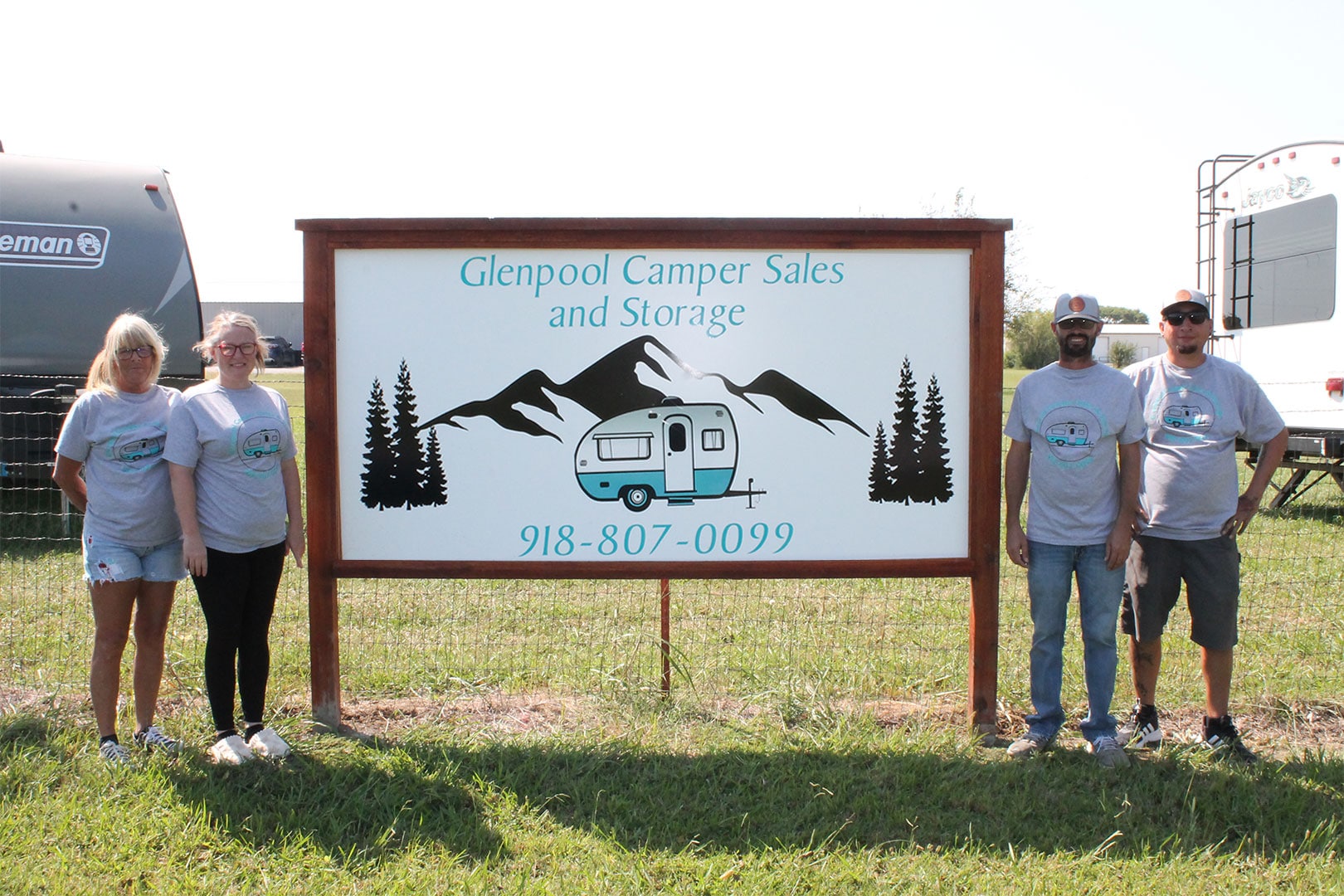 Glenpool Camper Sales & Storage team standing beside business sign with camper logo and phone number
