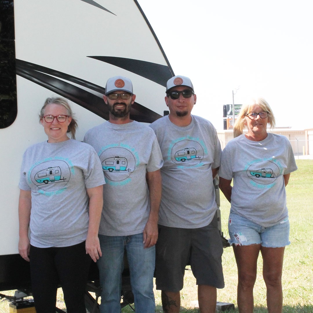 Glenpool Camper Sales & Storage team standing in front of RV wearing matching gray t-shirts with camper logo
